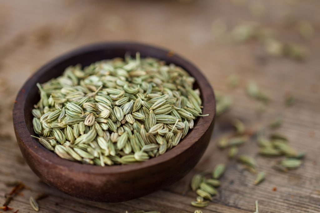 Semillas secas de hinojo sobre una superficie de madera, listas para infusión o siembra.